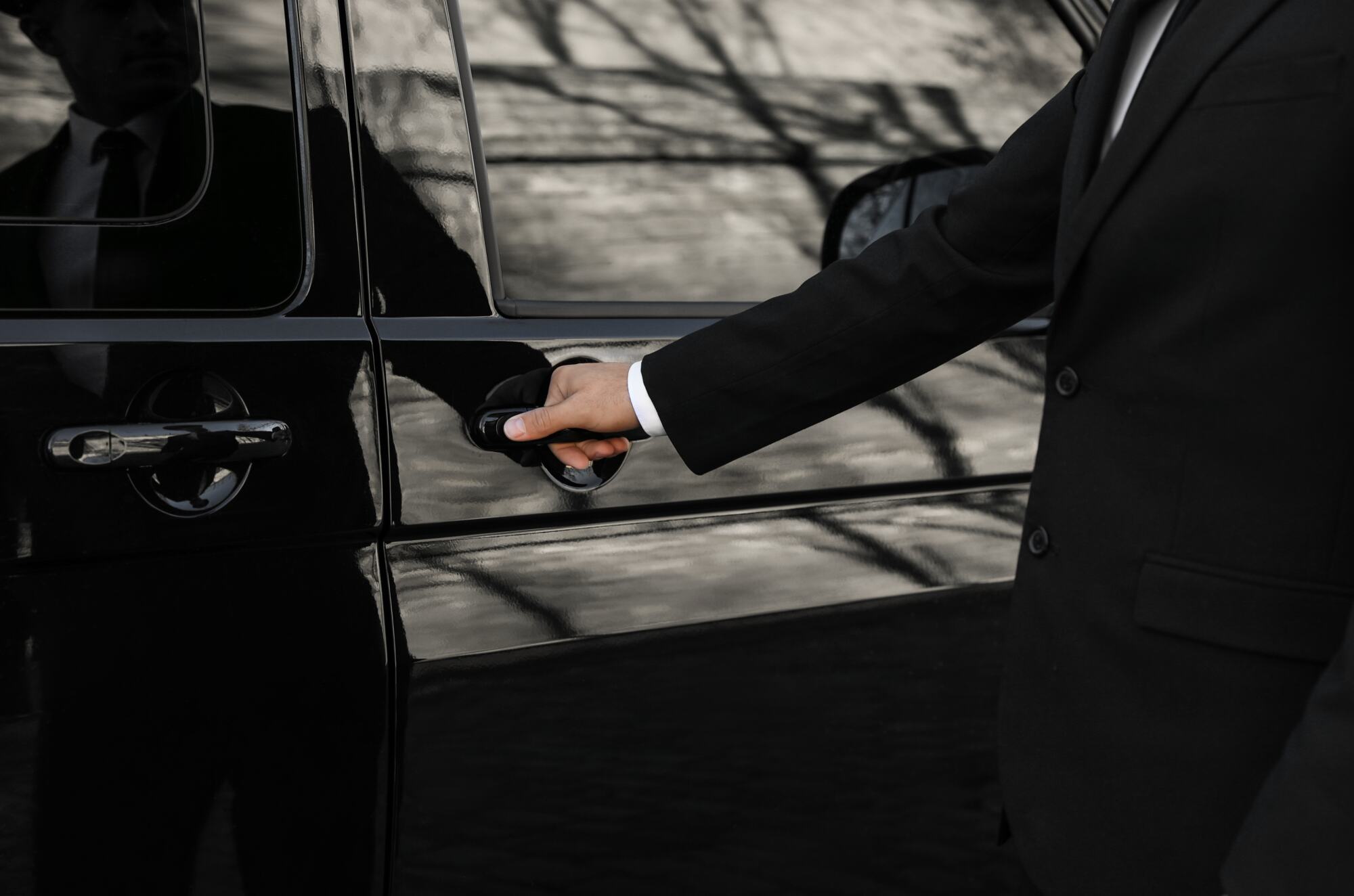 Conductor de traje abriendo la puerta de una van negra
